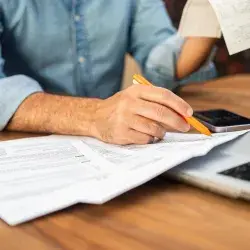 Hombre en camisa de mezclilla calculando impuestos con Comprobante y formas en un escritorio de madera. Concepto de preparación de impuestos y gestión financiera
