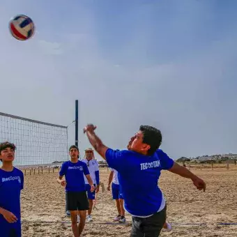 Alumnos jugando en equipo voleibol en la playa