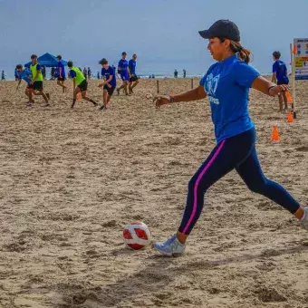Alumna pateando balón de fútbol en la playa