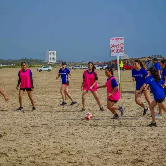 Alumnas jugando fútbol en equipo en la playa