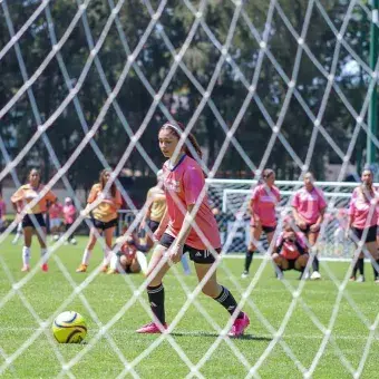 Vista de una jugadora de futbol a través de la red de la portería. 