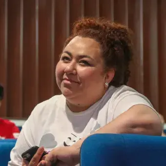 Mujer sosteniendo micrófono en sus manos, sentada en una butaca.