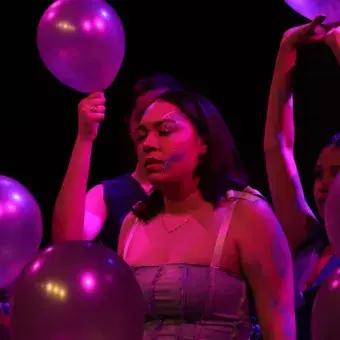 Chica en escena rodeada de personas sosteniendo globos. 