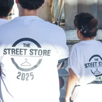 Vista de espaldas de tres voluntarios portando camisetas blancas con un logo que dice Street Store 2025.