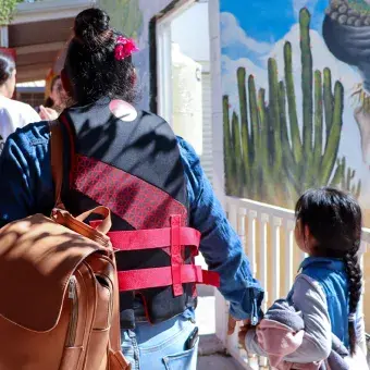 Vista de espaldas de una mujer caminando de la mano de una niña. 