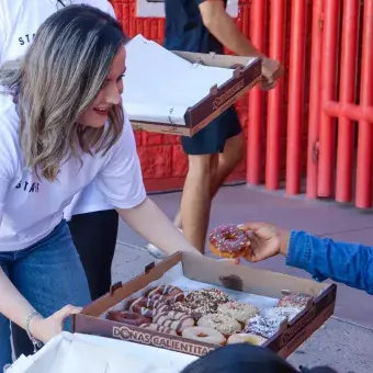 Mujer repartiendo donas a personas sentadas en sillas. 