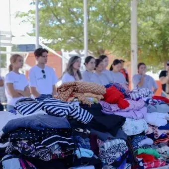 Mesas con ropa doblada y apilada con personas formadas en el fondo. 