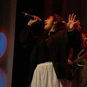 Chica cantando en escenario con top negro y falda blanca.