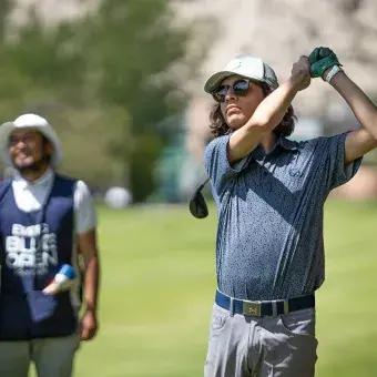 Jugador realiza su swing de golf mientras dos caddies observan al fondo con chalecos del torneo EXATEC Blue Open, realizado en el Club de Golf Pachuca en beneficio de Líderes del Mañana.