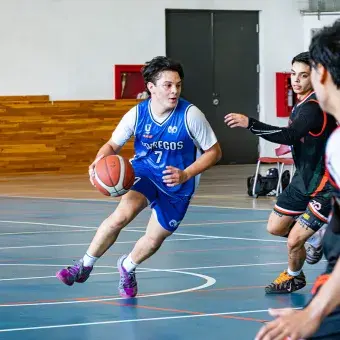 Un jugador de básquetbol esquiva a su contrincante mientras bota el balón.