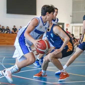 Un jugador de básquetbol esquiva a su contrincante mientras bota el balón.