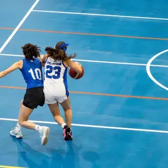 Vista desde lo alto de dos jugadoras de básquetbol en la cancha mientras una trata de esquivar a la otra con el balón.