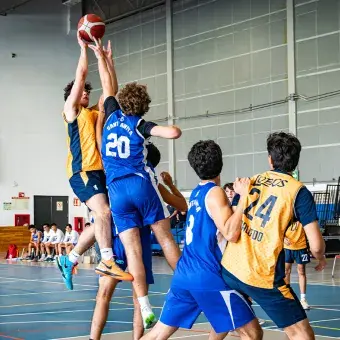 Un jugador de básquetbol salta para hacer un tiro mientras su contrincante salta para bloquear el tiro. 