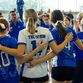 Jugadoras de voleibol de espaldas abrazadas en círculo.