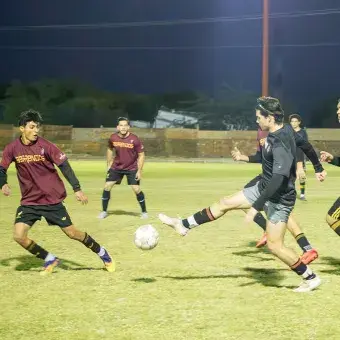 Jóvenes jugando fútbol por la noche en una cancha. 