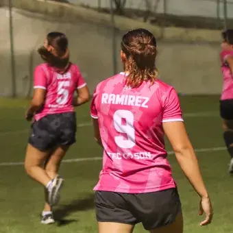 Vista de la espalda de una jugadora de fútbol portando un uniforme rosa. 