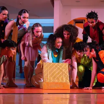 Actores con vestuarios y narices de payaso alrededor de una caja.