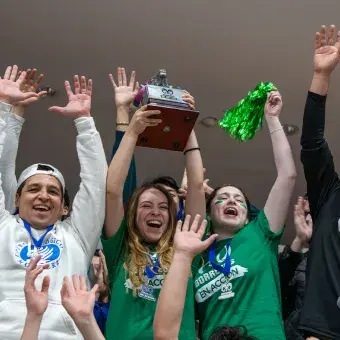 Grupo de estudiantes y profesores celebrando y sosteniendo un trofeo en el aire. 