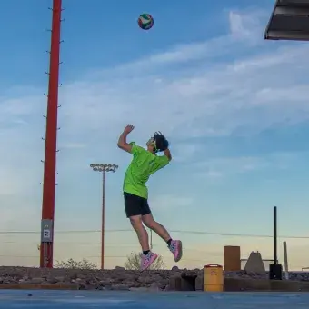 Vista de perfil de alumno saltando para hacer un saque de voleibol. 